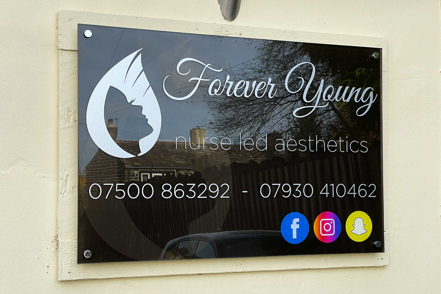 Forever Young nurse-led aesthetics clinic sign with silver logo and contact details on gloss black acrylic panel