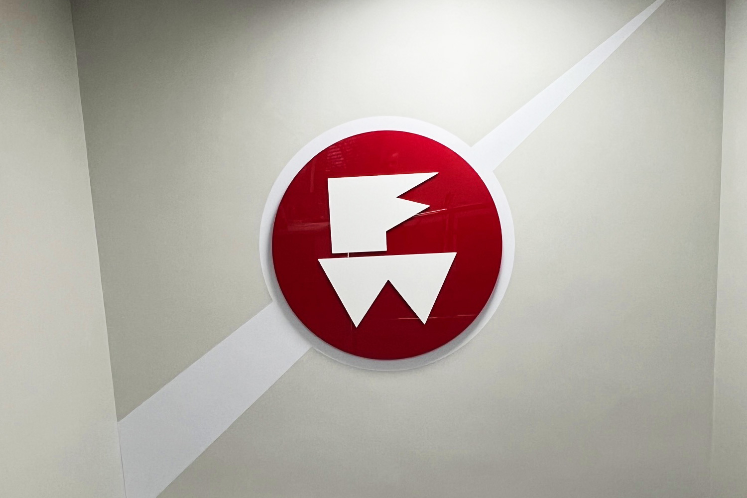 A sleek 3D logo sign featuring bold red and white elements, professionally installed on a feature wall in a corporate space