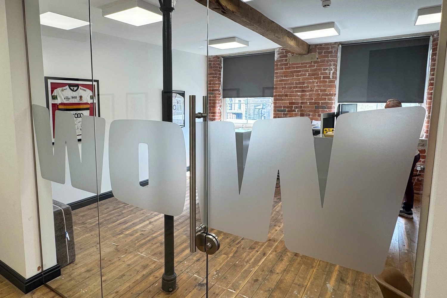 Large frosted vinyl lettering spelling "WOW" applied to internal glass office doors with exposed brick and wooden flooring interior