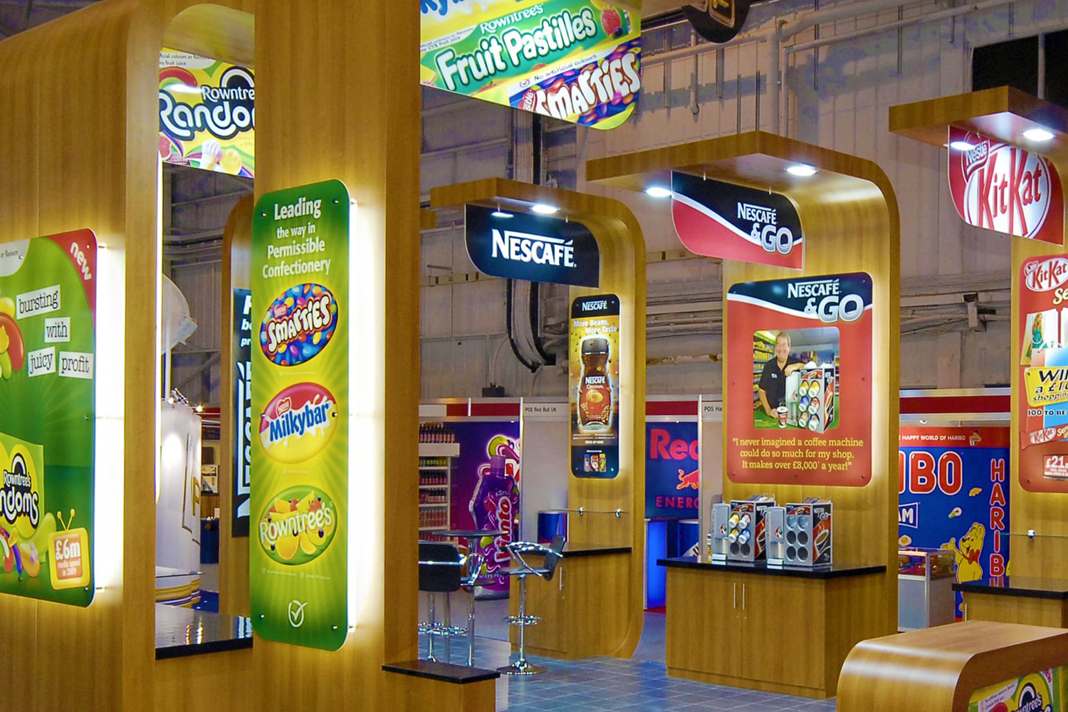 Colourful exhibition stand featuring Rowntree’s, Smarties, Milkybar, and Nescafé branding with illuminated product displays and curved wooden panels