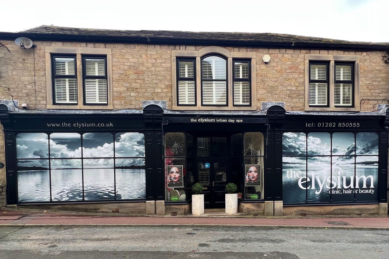 Elegant shop front for The Elysium urban day spa with monochrome lake scene window graphics and bold branding on traditional stone building