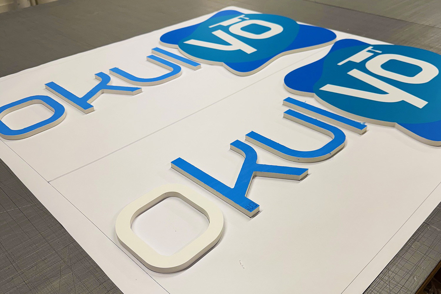 Blue and white router-cut acrylic sign letters laid out on a worktable for assembly