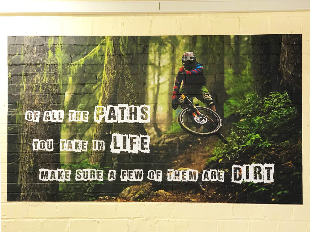 Motivational wall graphic featuring a mountain biker mid-jump in a forest with the quote “Of all the paths you take in life, make sure a few of them are dirt,” produced by G4 Graphics in Leeds